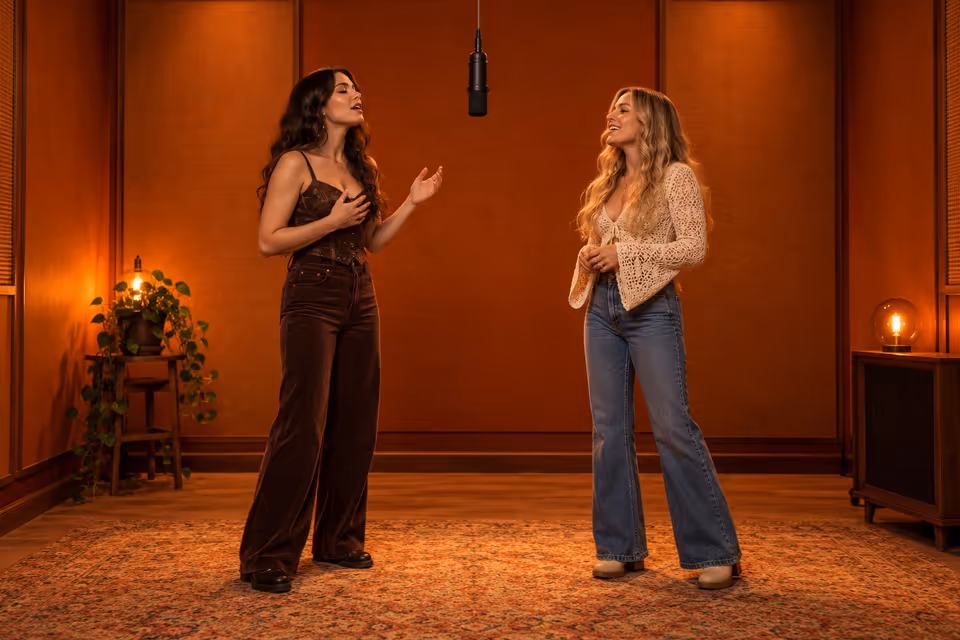 Two women taking turns at a hanging microphone in an orange recording booth